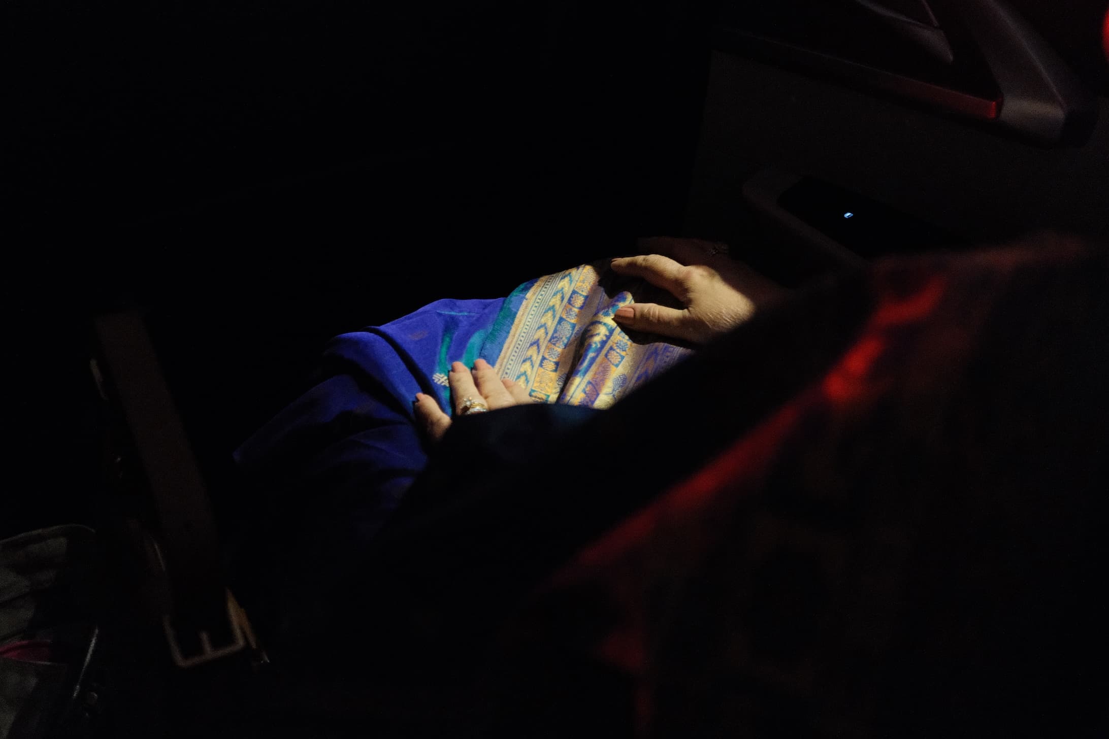 Woman wearing blue saree with gold embroidered border, hands visible against dark background