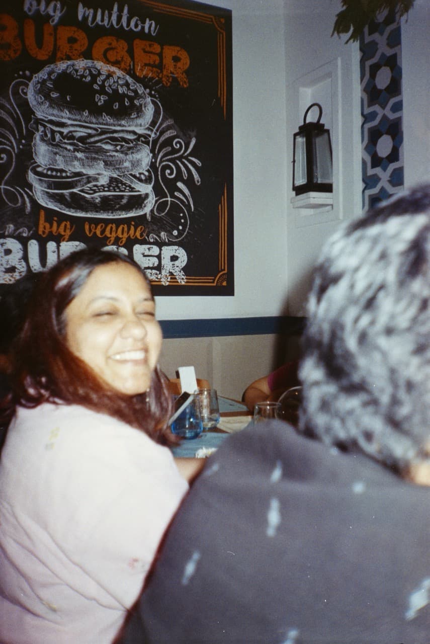 Woman smiling at restaurant table with burger menu sign and hanging lantern in background in vintage film photograph