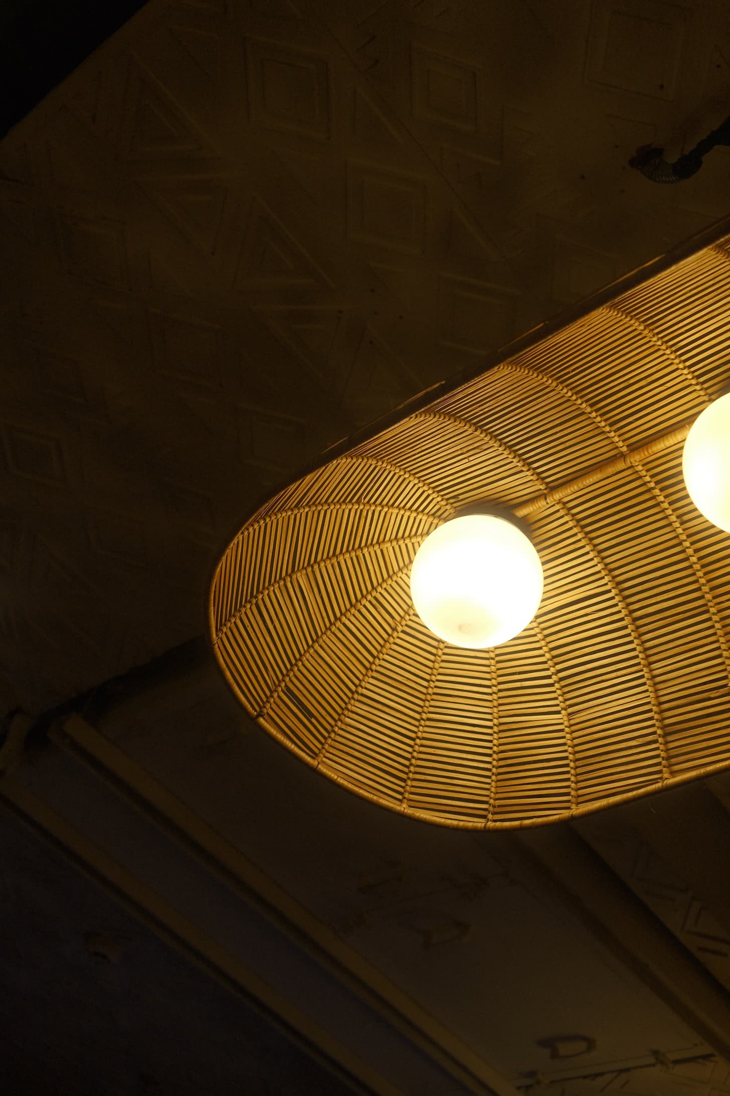 Woven wicker pendant light fixture with warm glowing bulbs against dark ceiling