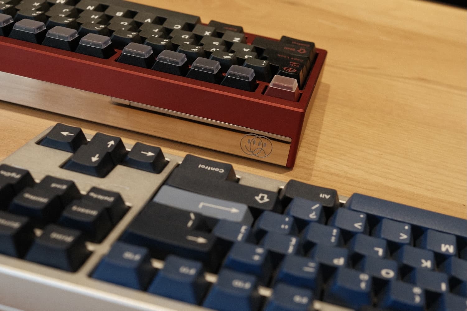 Two mechanical keyboards with red and blue cases and black keycaps on wooden surface at keyboard meetup