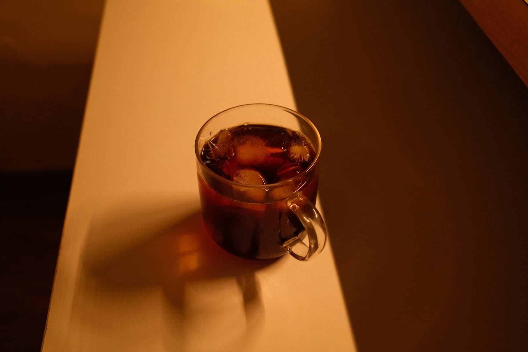 Glass mug of iced pour over coffee with ice cubes in warm golden sunlight with dramatic shadows