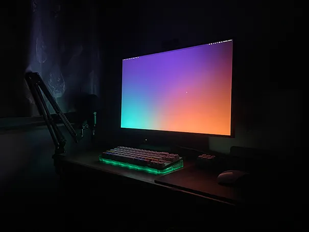 A desk with a large LED monitor, Apple Magic Mouse and a custom built mechanical keyboard with a microphone on a Mic stand clipped to the table